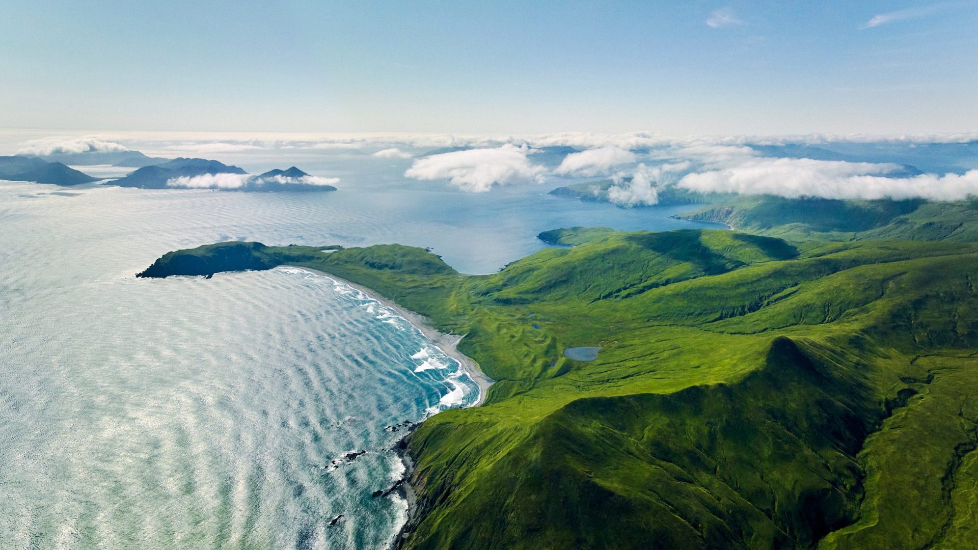 Birds eye view of green island chain, low hanging white cloud and blue waters