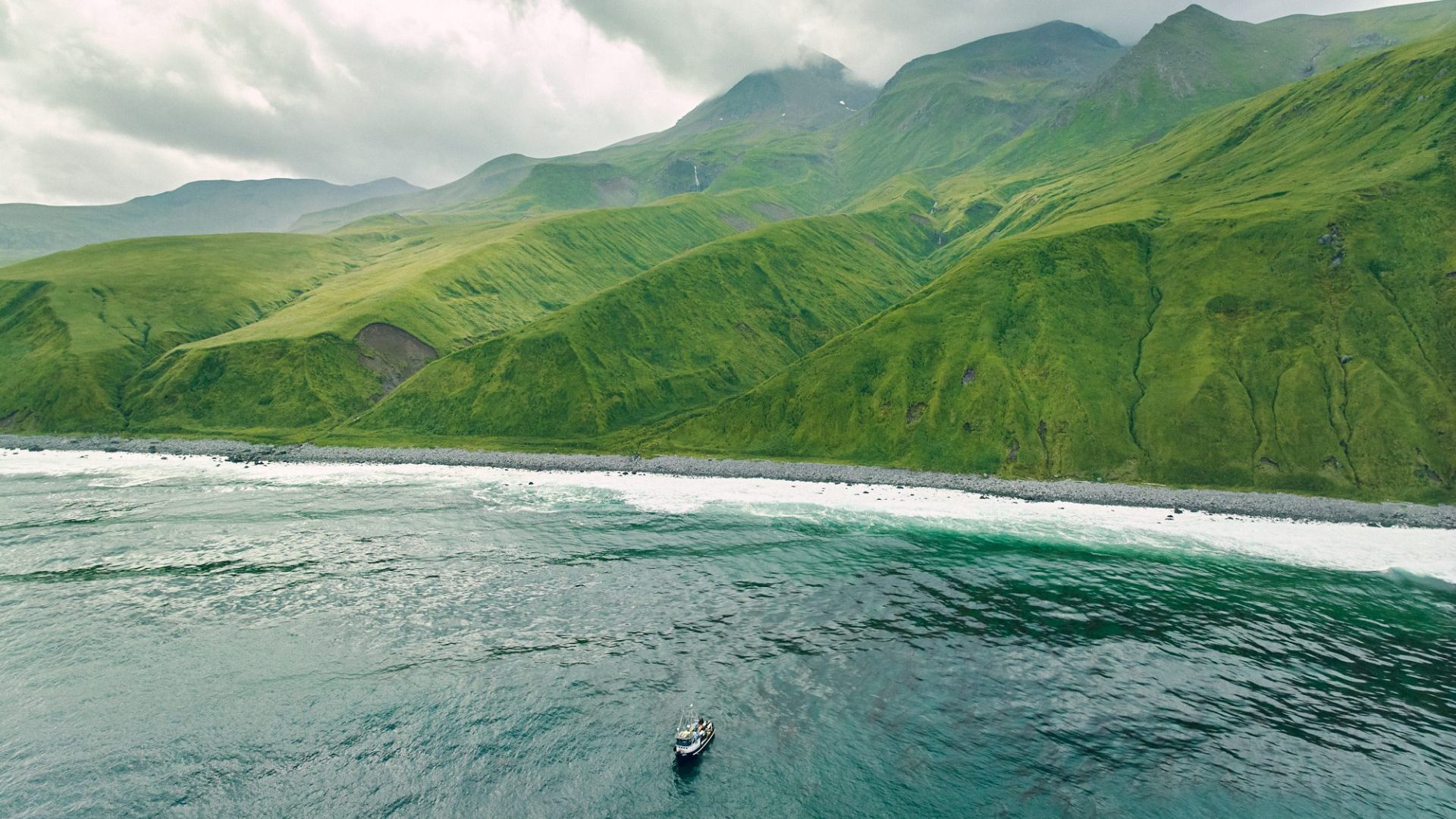 Boat heads towards beach with green rolling hills