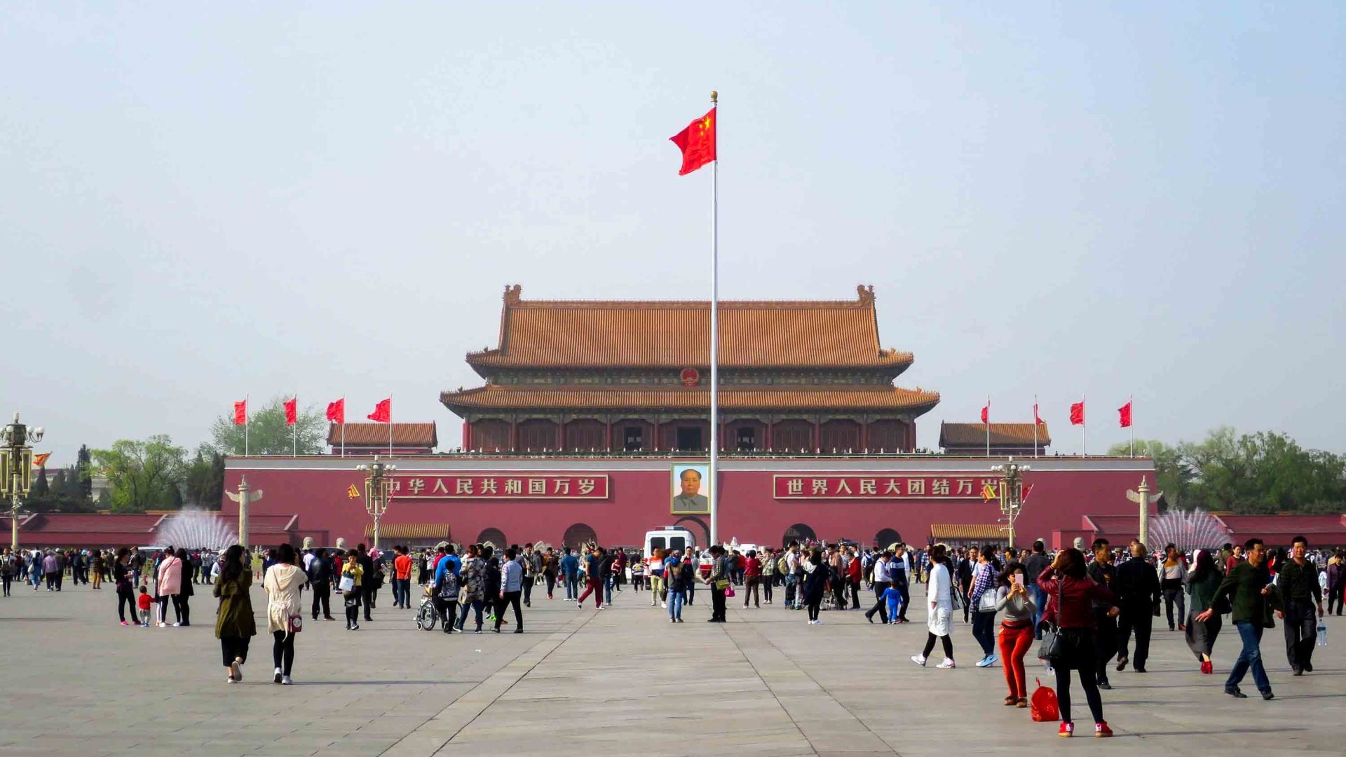 A building with a flag out the front and lots of people walking round it.