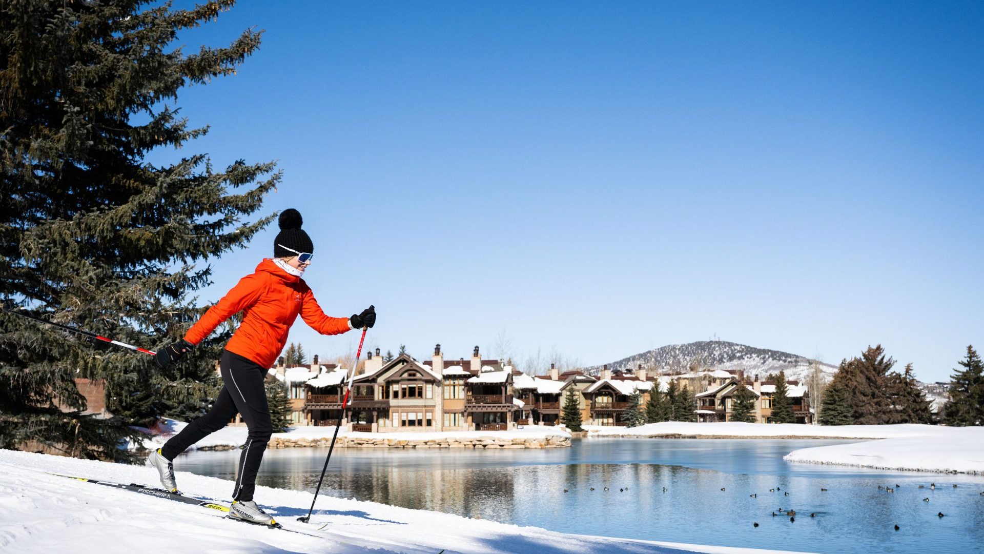 Woman in red snow jacket skis past lake