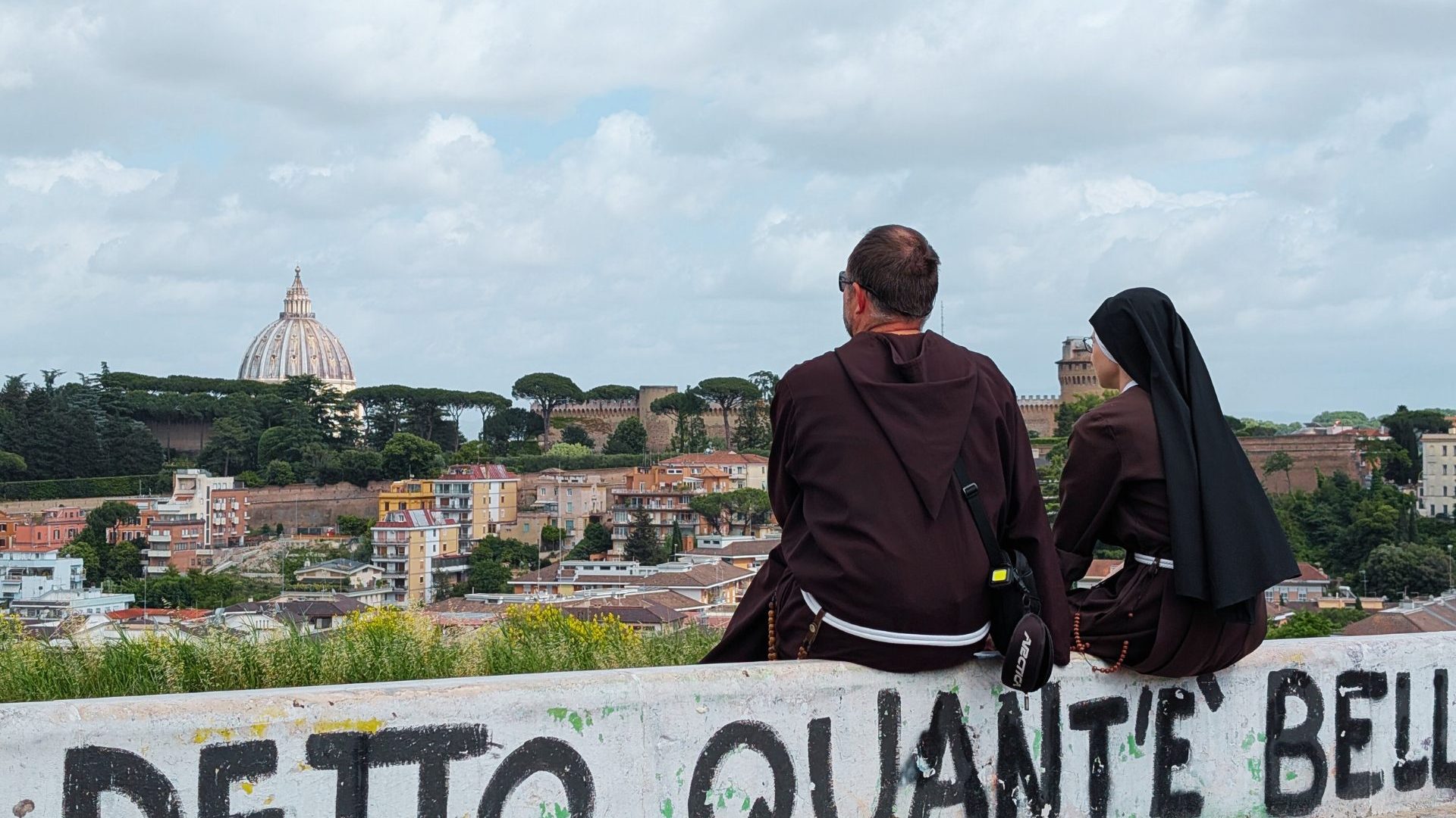 Monk and nun sit on graffiti'd wall overlooking Vatican City