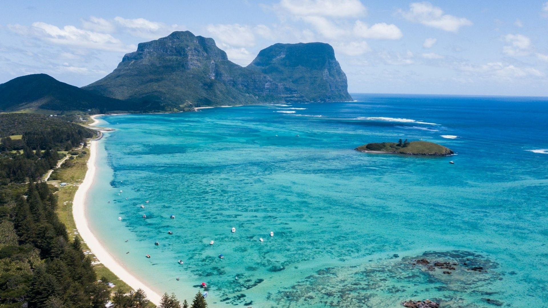A beautiful white-sand beach along a bay lapped by sparkling aquamarine water with rocky outcrops in the background.