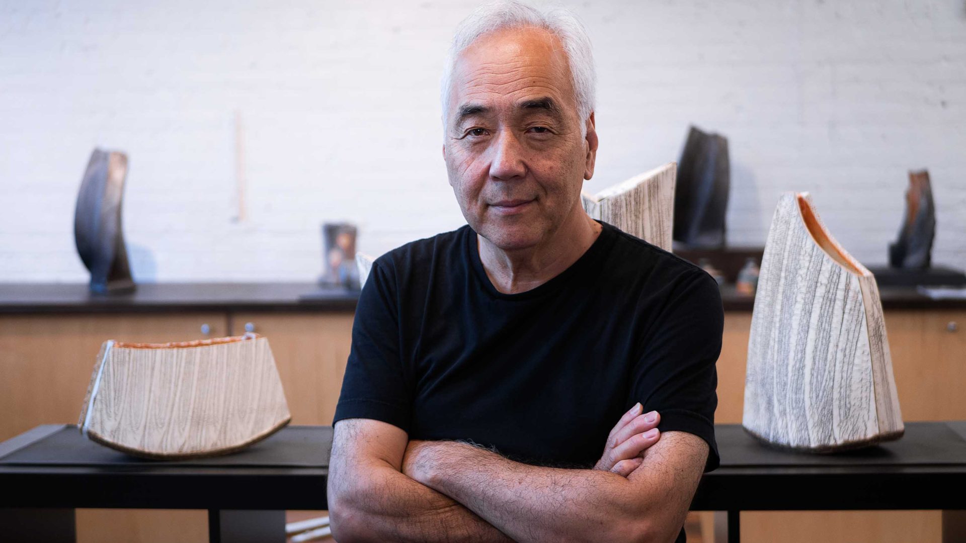 A man smiles and poses besides ceramics he has designed