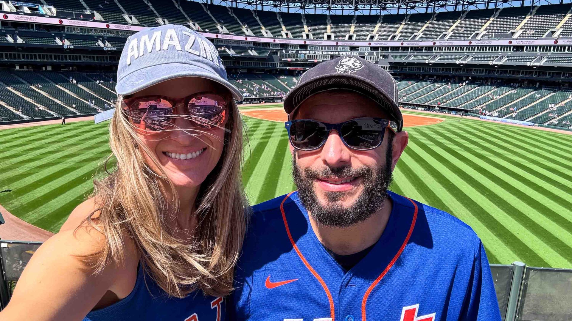 A man and woman smile in front of a baseball field.
