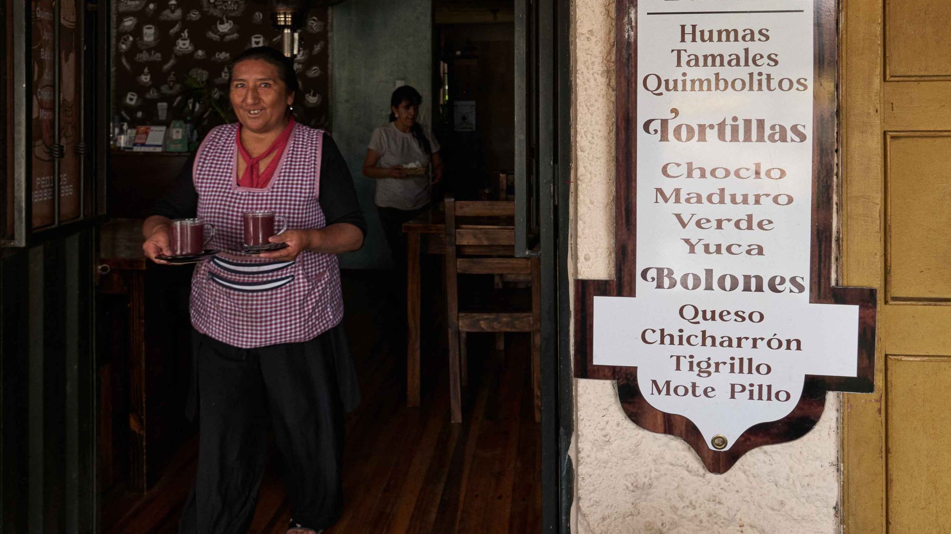 A woman carries two drinks outside a restaurant.