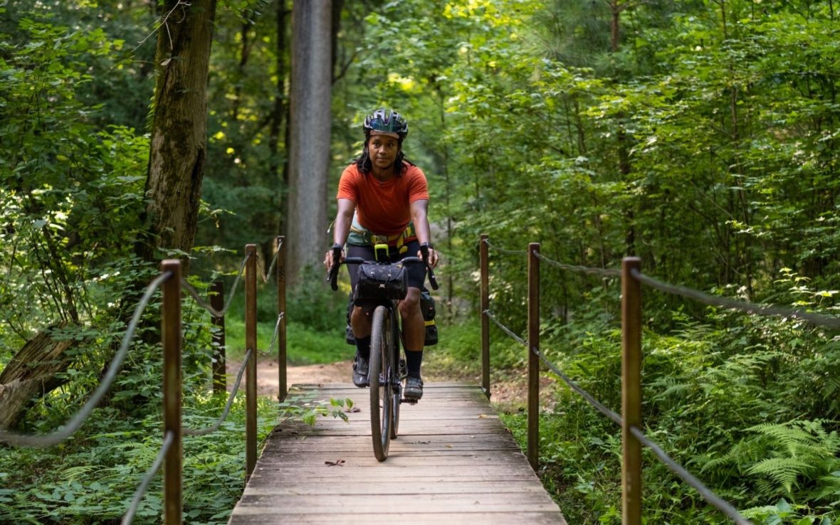 A woman in a red top cycles through woodland