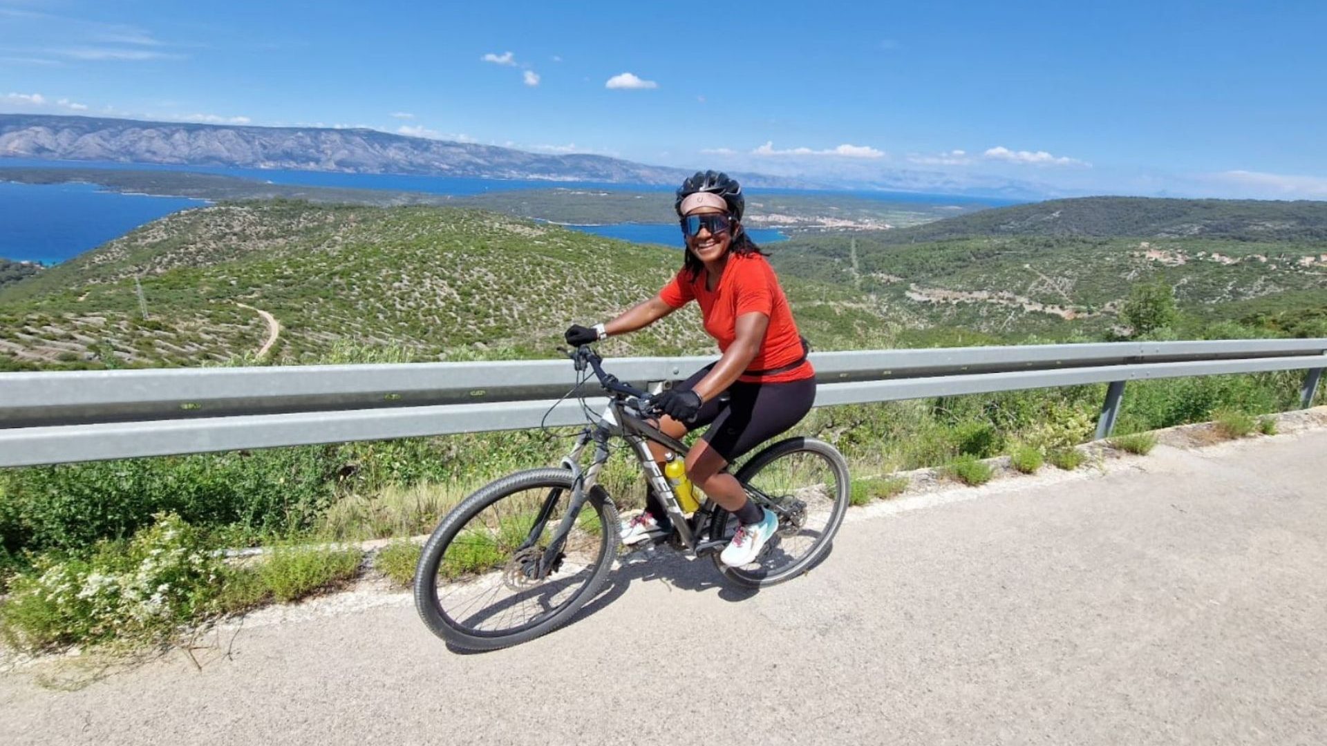 A cyclist in a red top cycles along a coastal road