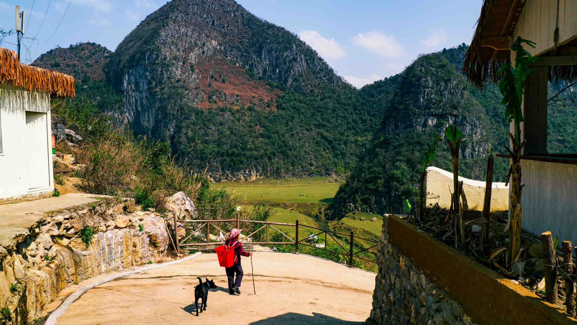 A person walks along the road, followed by a dog, and surrounded by tall cliffs.