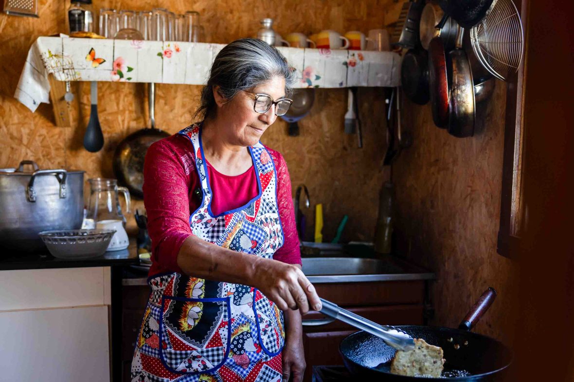 A woman prepares a round fried food in a pan, inside her homely kitchen.
