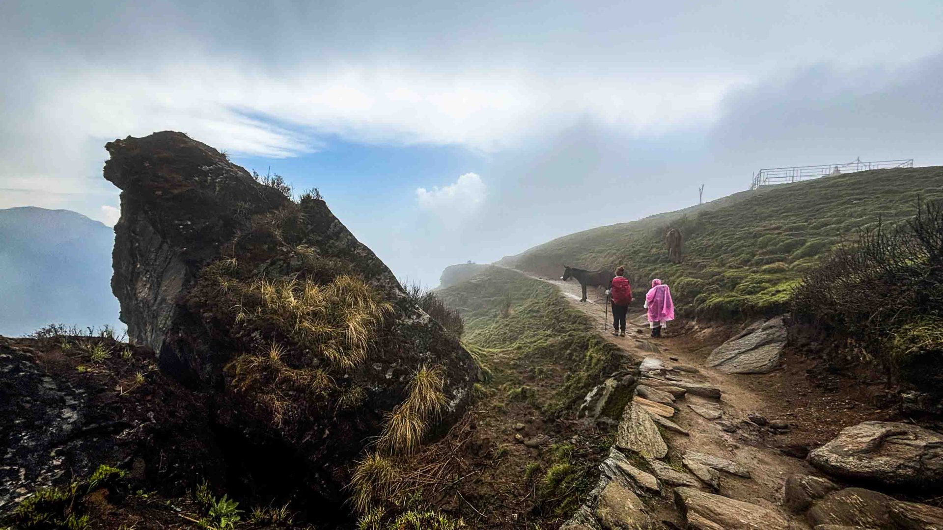 A person walks along a trail below a very cloudy sky.