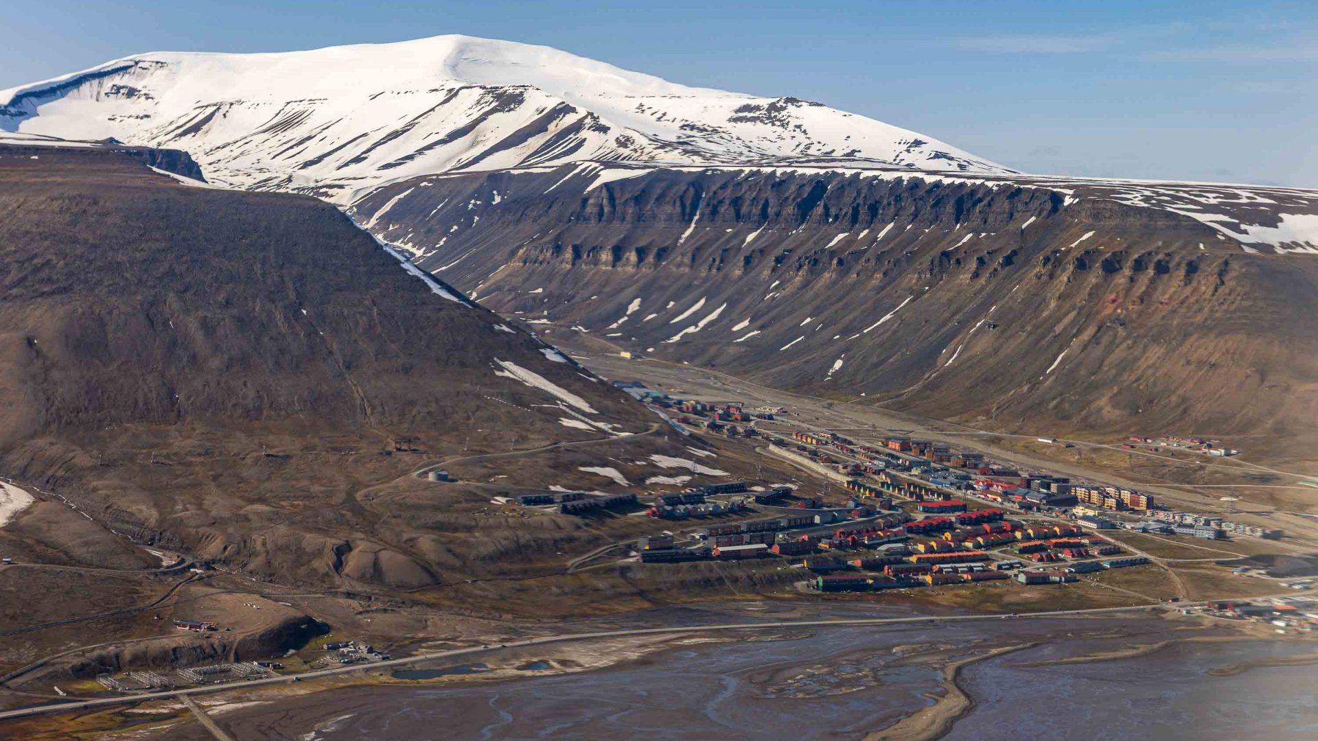 Bare mountains slope down to a town on the edge of water.