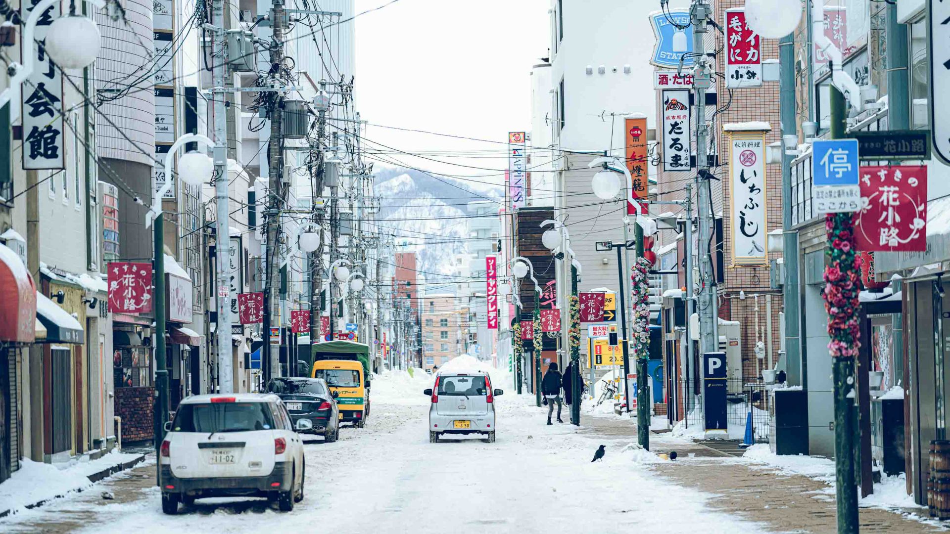 A car drives up a snowy Japanese street toward a mountain.