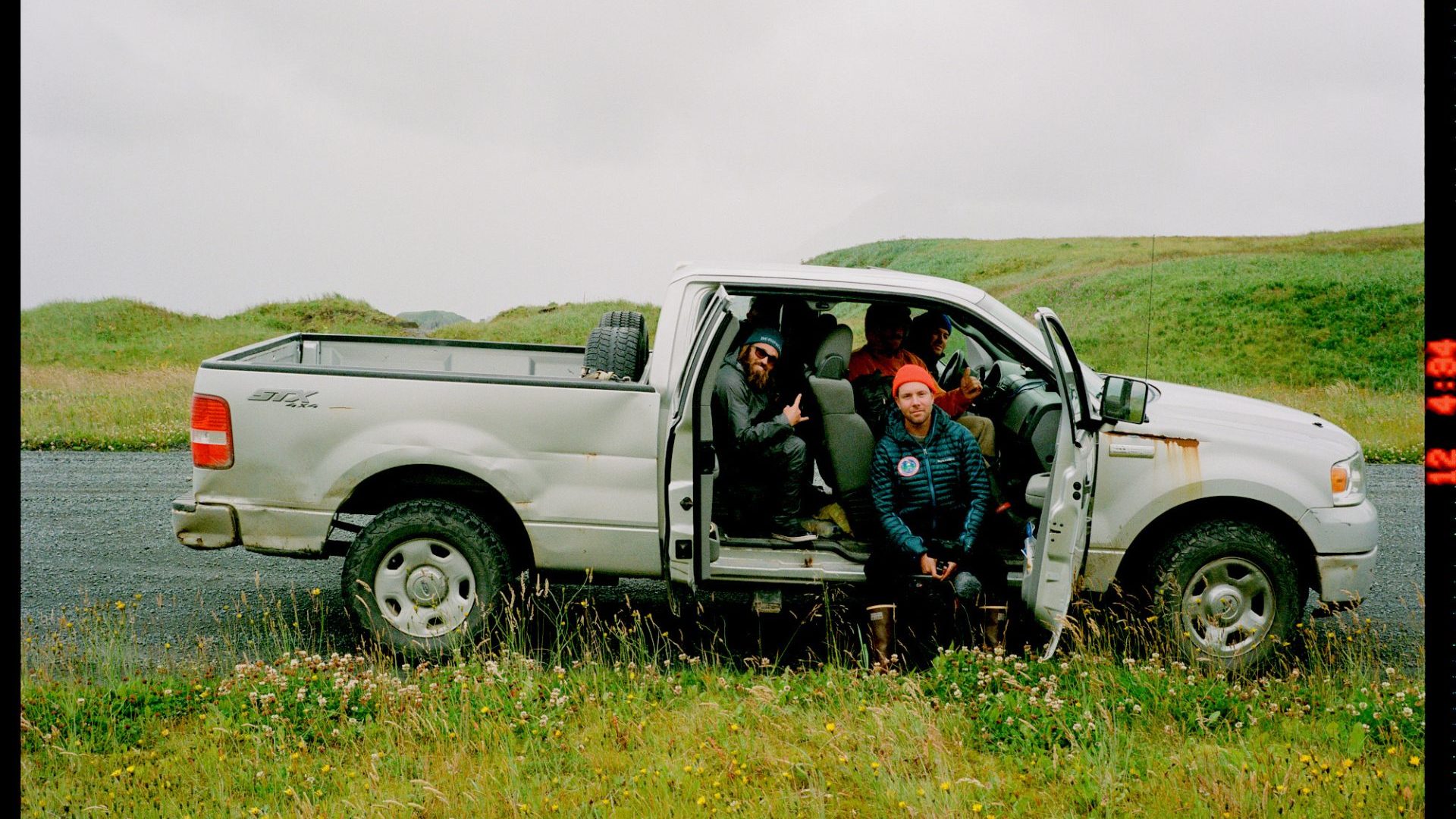 Group of men sit in truck, smiling at camera.