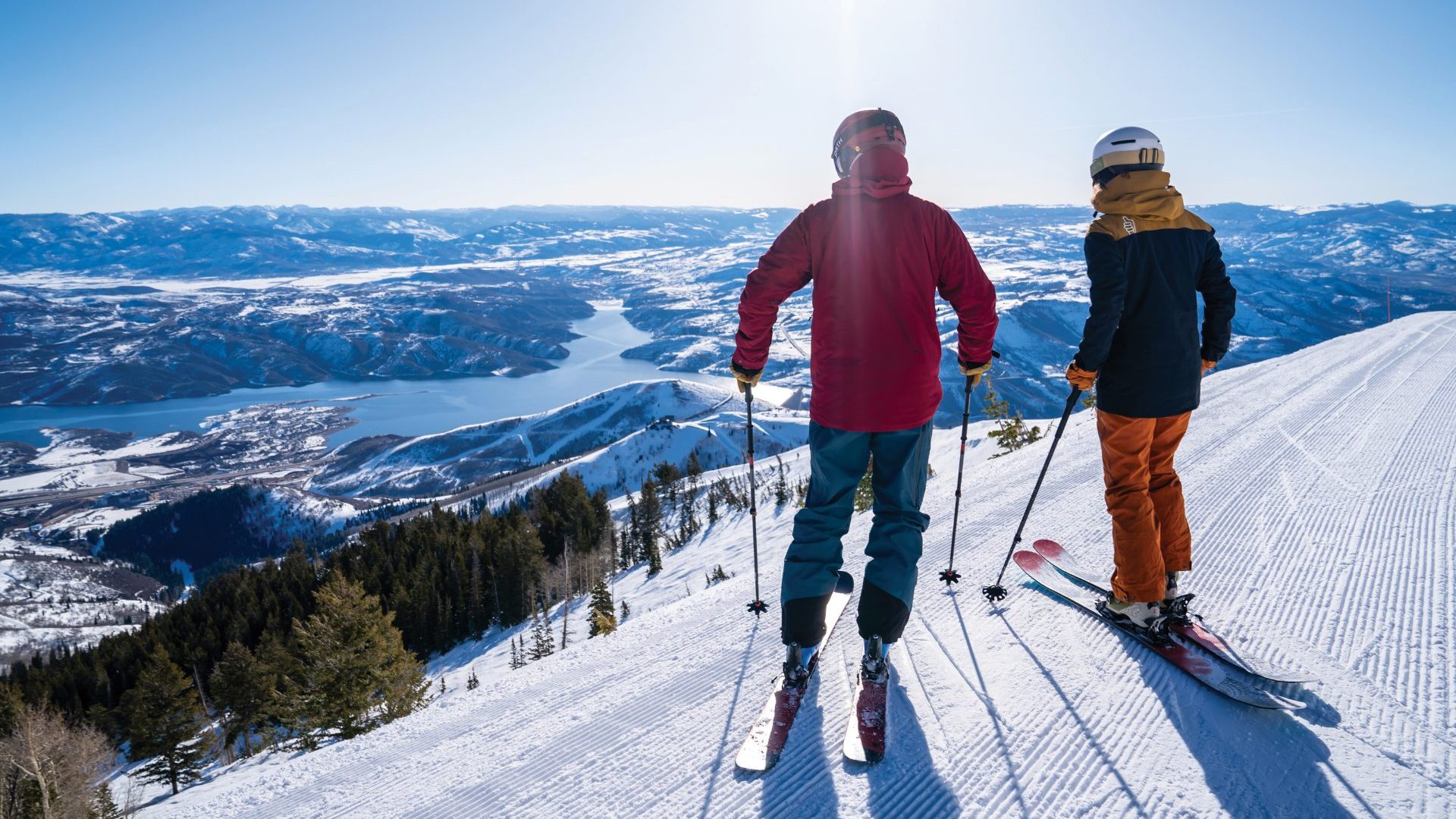 Two skiers are silhoutted looking down on lake