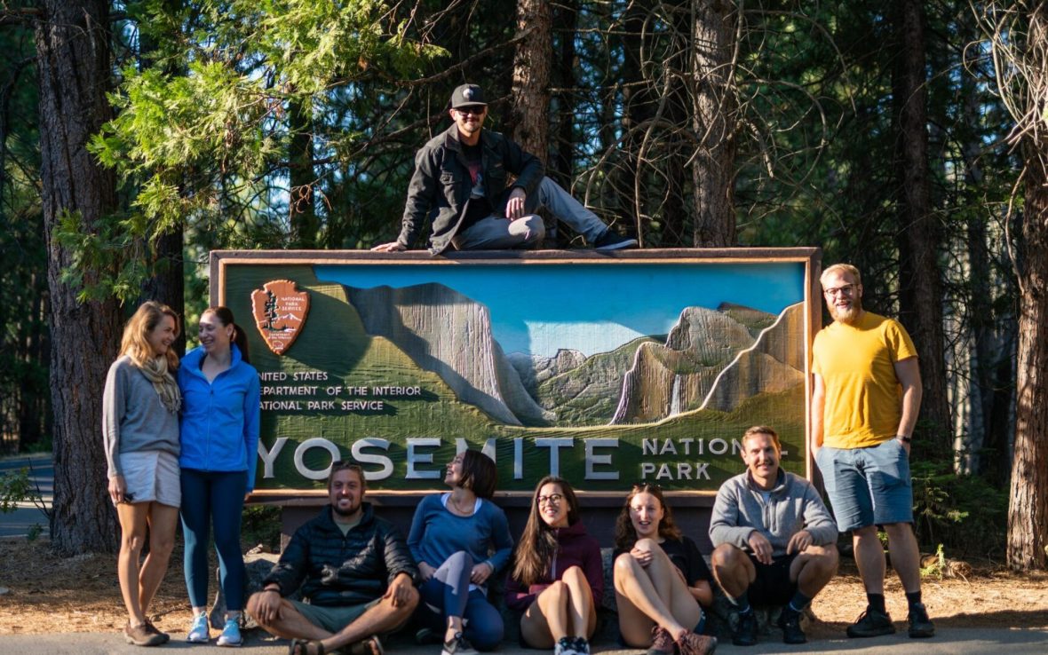 Group of travelers stand in front of Yosemite entrance sign