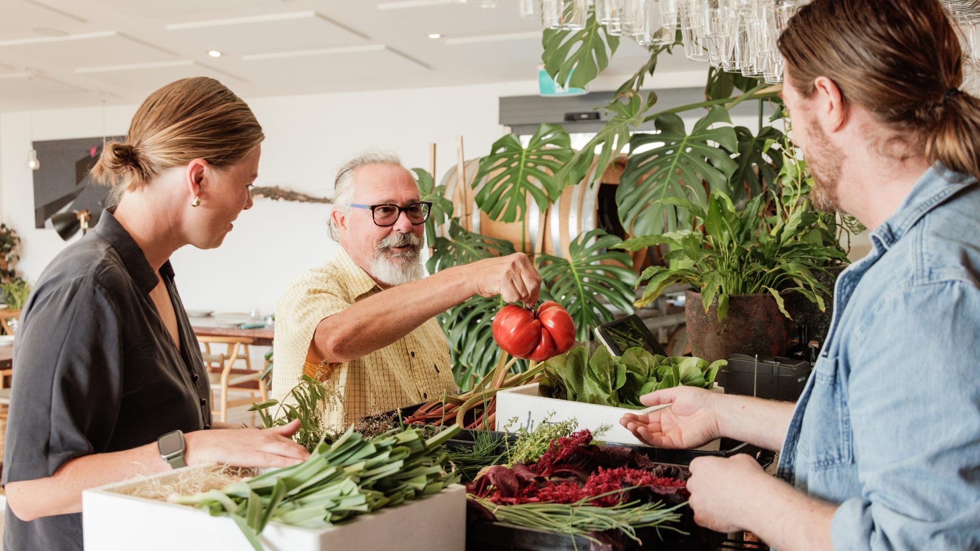 Three people smile and chat at a vegetable stand