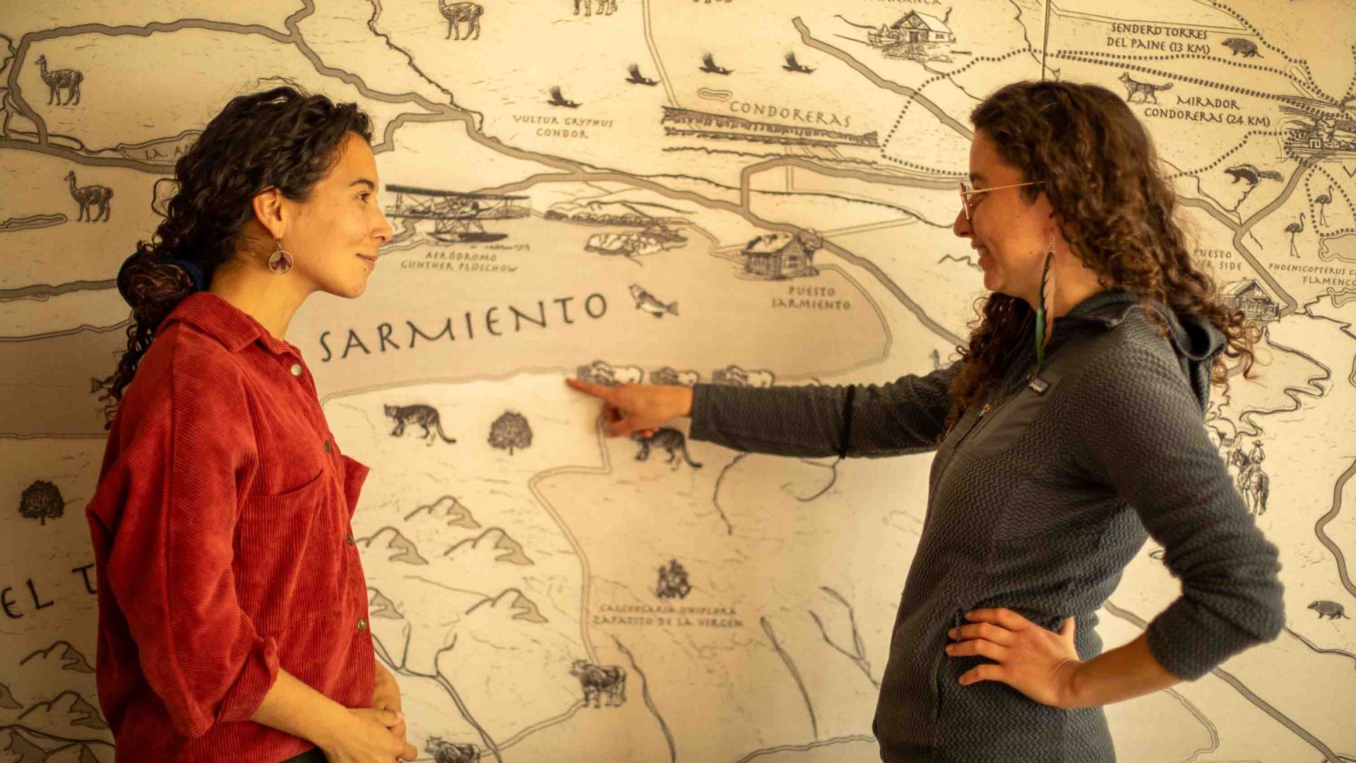 Two women point to a map.