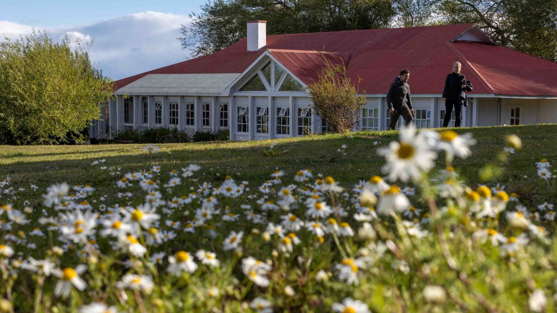 A building with white walls and a terracotta roof in a garden of flowers.