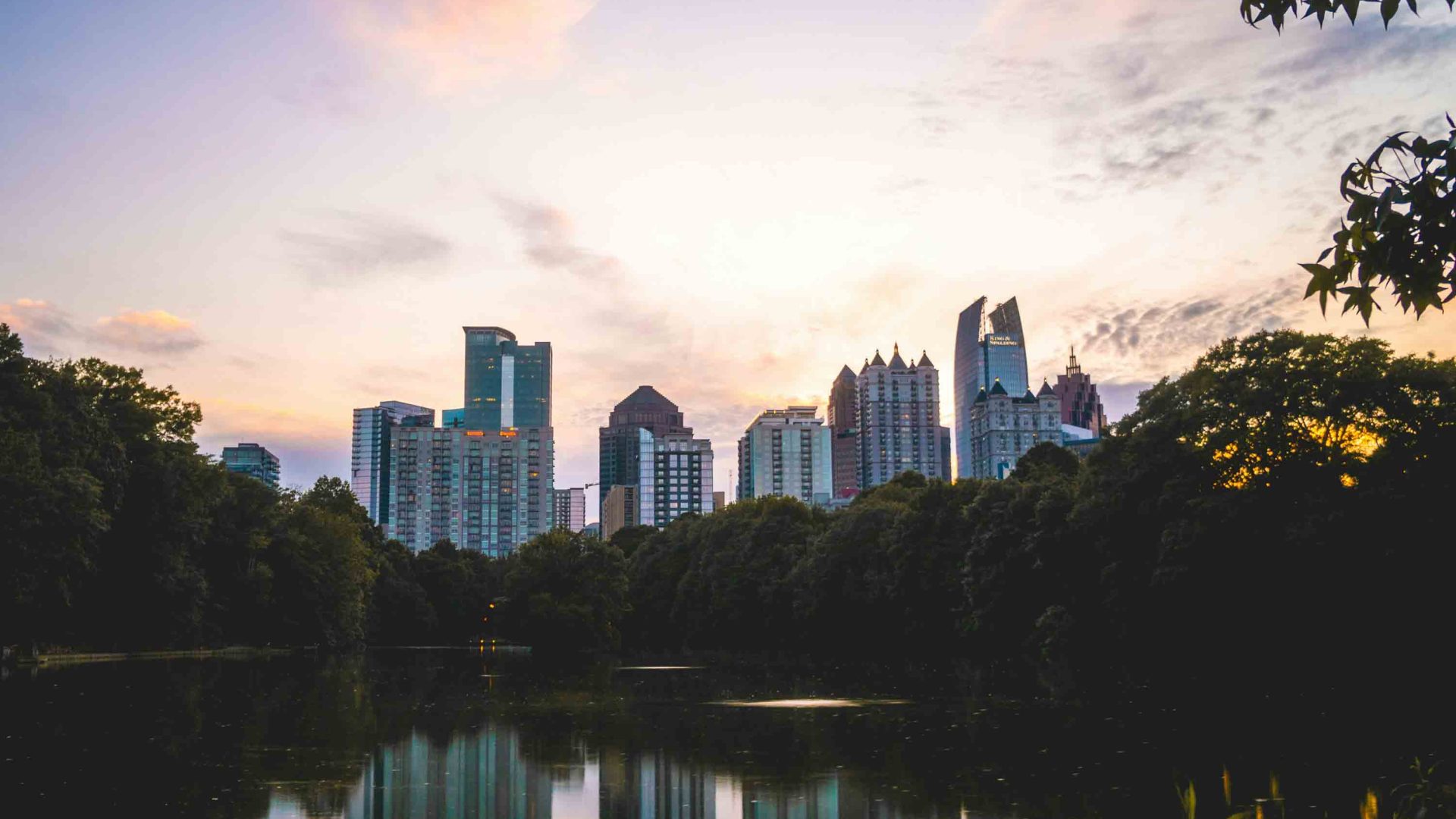 Buildings are reflected in a tree fringed lake.