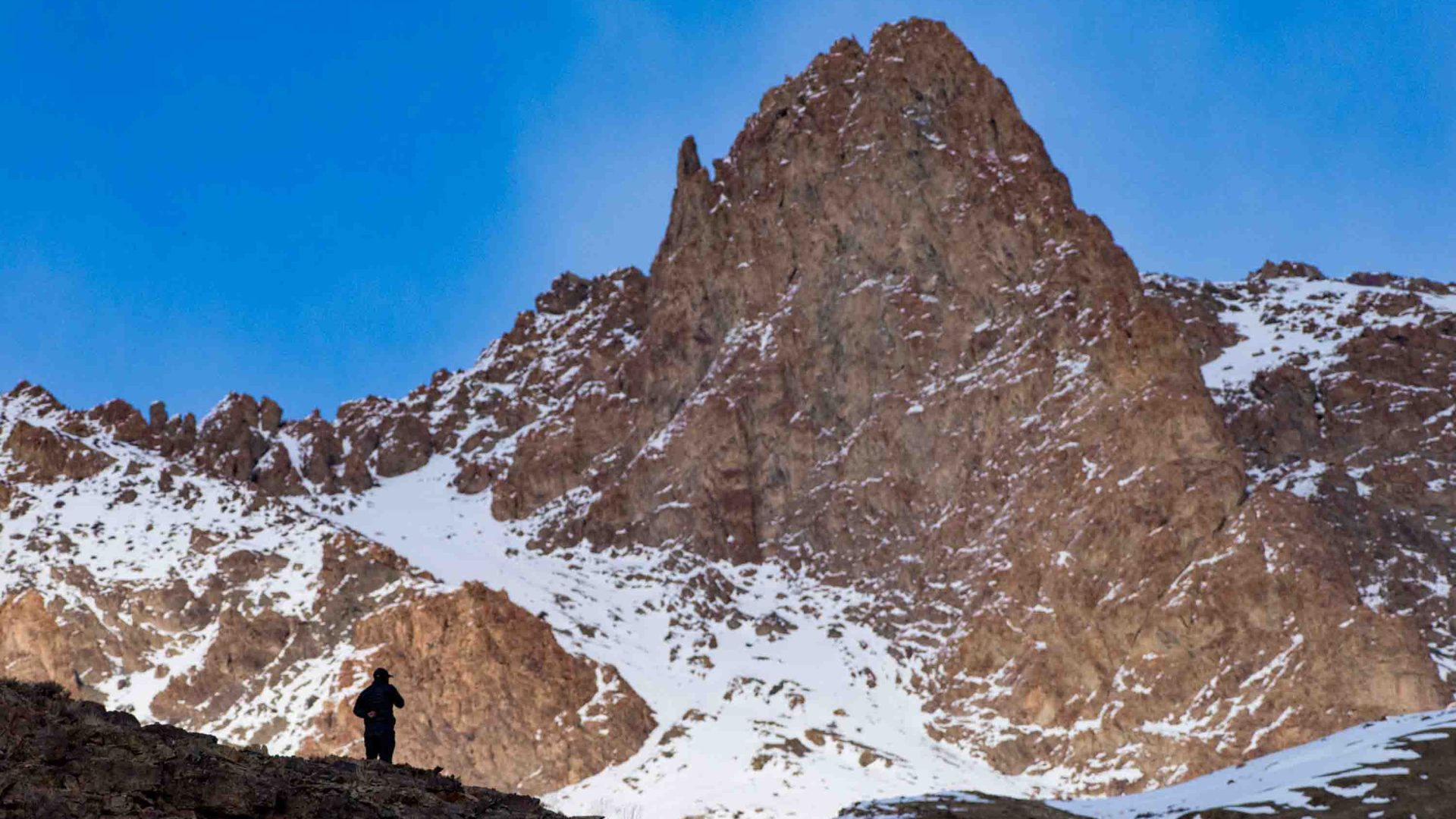 The silhouette of a person looking out at a mountain.