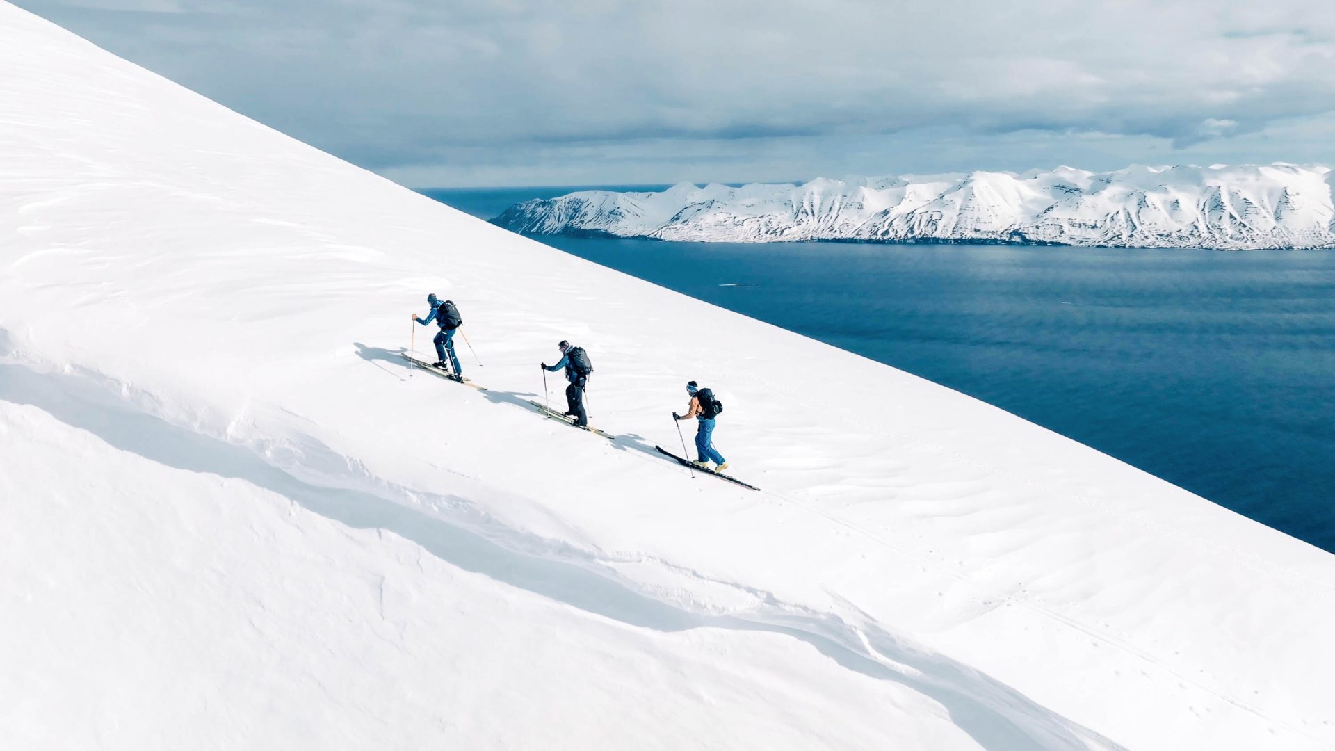 People do cross country skiing on a hill with icebergs in the distance.