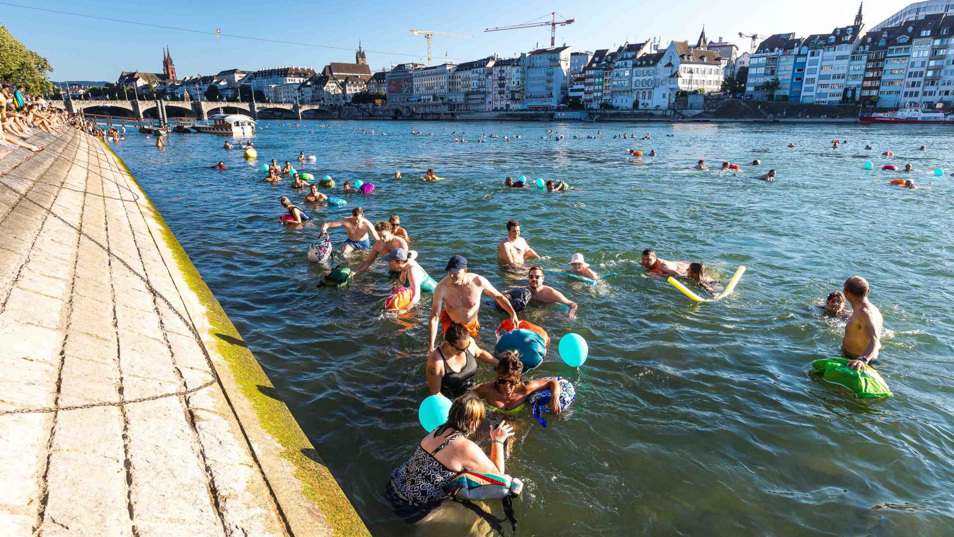 People swim in a river alongside the bank.