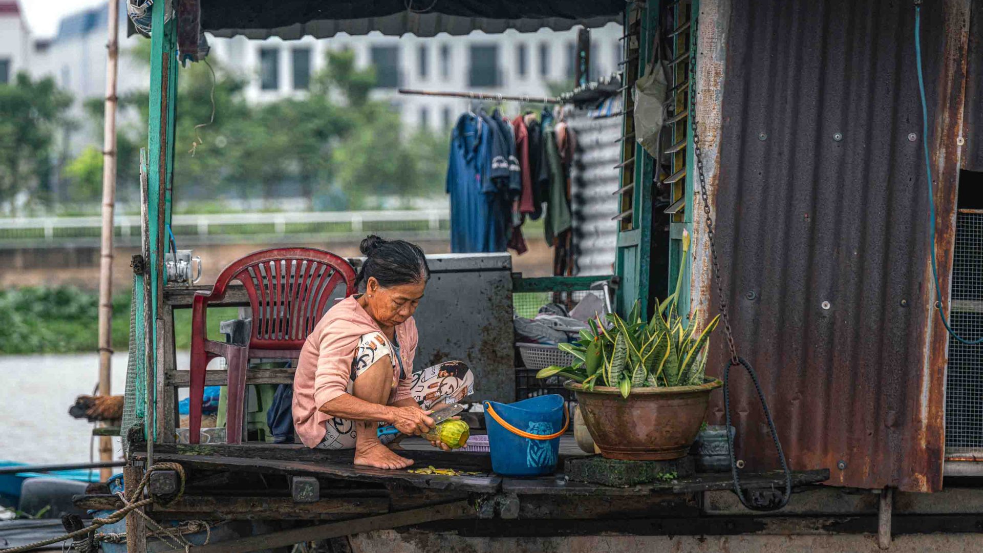 A woman cuts fruit while crouched down on her boat.