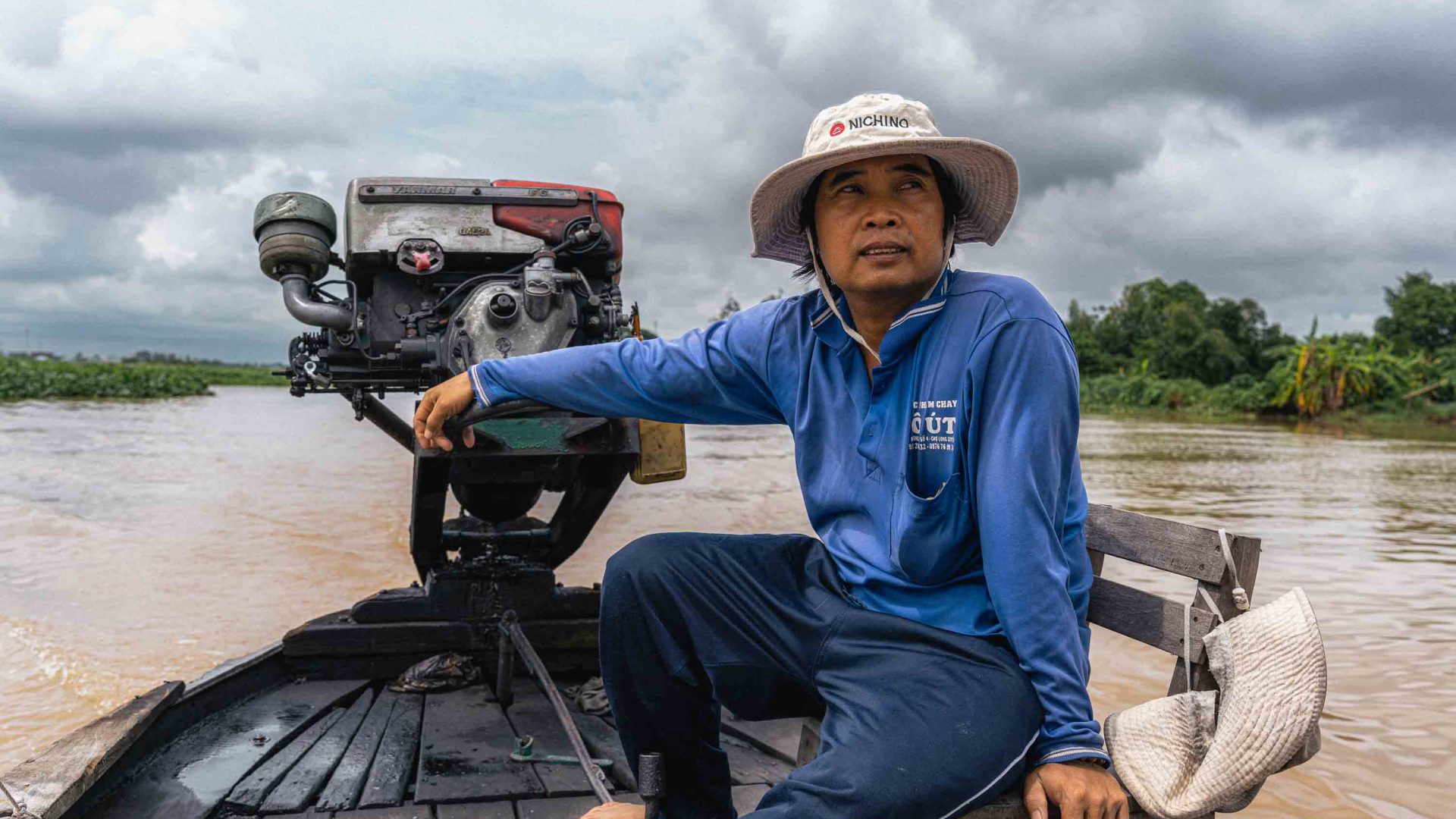 A man in a blue shirt steers a boat through water.